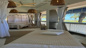 Habitación de hotel con dos camas, un ventanal con vista a palmeras y al mar, y lámparas colgantes de mimbre.
