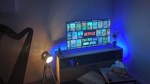 A living room with a flat-screen TV displaying a Netflix interface, a lamp, a small table, and a harp. - 2P gîte with sauna on the Route des Vins near Colmar (Bergheim)