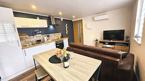 A modern kitchen with white cabinets, a dining table with a bottle of champagne, and a brown leather sofa in a living area with a TV. - 2P gîte with sauna on the Route des Vins near Colmar (Bergheim)