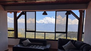 A room with a large window offering a mountain view, a black leather sofa, and a dark armchair.