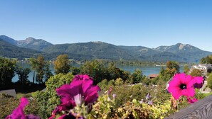 A lake with mountains in the background, a wooden deck, and pink flowers in the foreground. - Apartment Multicolor Amethyst at Wolfgangsee Alpenblick (St. Wolfgang)