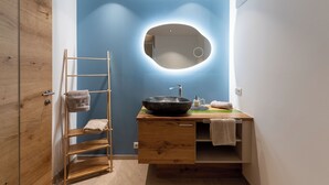 Ein Badezimmer mit blauer Wand, einem hölzernen Waschtisch, einem runden Spiegel und einem Handtuchhalter.