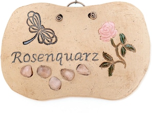 Um objeto decorativo com a palavra 'Rosengartz' e uma borboleta, rosa e folhas.