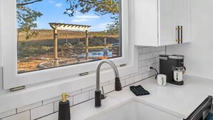 Eine Küche mit Fenster, weißen Schränken, einem Edelstahl-Wasserhahn, einer Kaffeemaschine und einem Spülbecken.