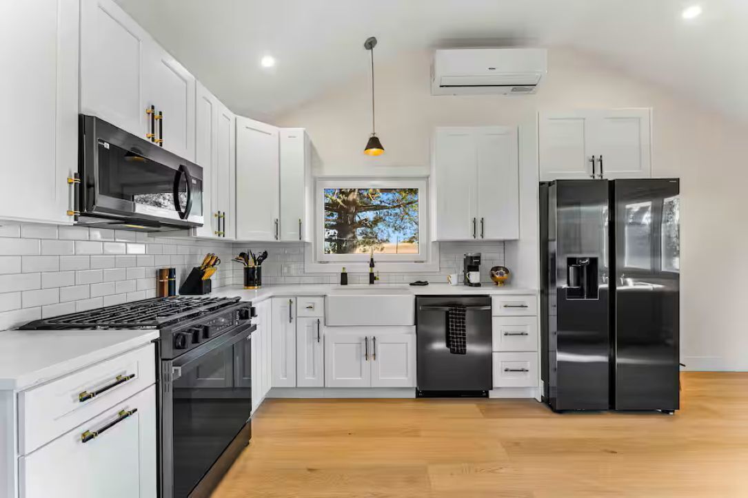 A modern kitchen with white cabinets, stainless steel appliances, a black stove, and a window with a view of trees.