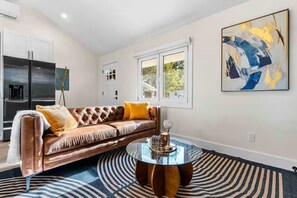 Un salon moderne avec un canapé en cuir, une table basse en verre et un grand tableau abstrait accroché au mur.