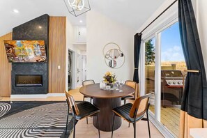 Un intérieur moderne avec une cheminée, une table à manger, des chaises et une grande fenêtre avec un grillage à l’extérieur.