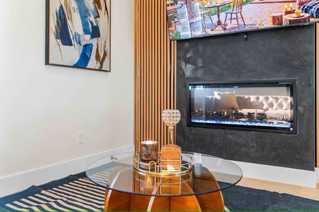 A modern living room with a fireplace, a glass coffee table, and a striped rug.