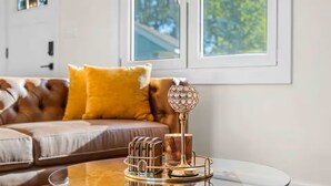 Ein Wohnzimmer mit Glastisch, dekorativem Metallständer und braunem Ledersofa mit gelbem Kissen.