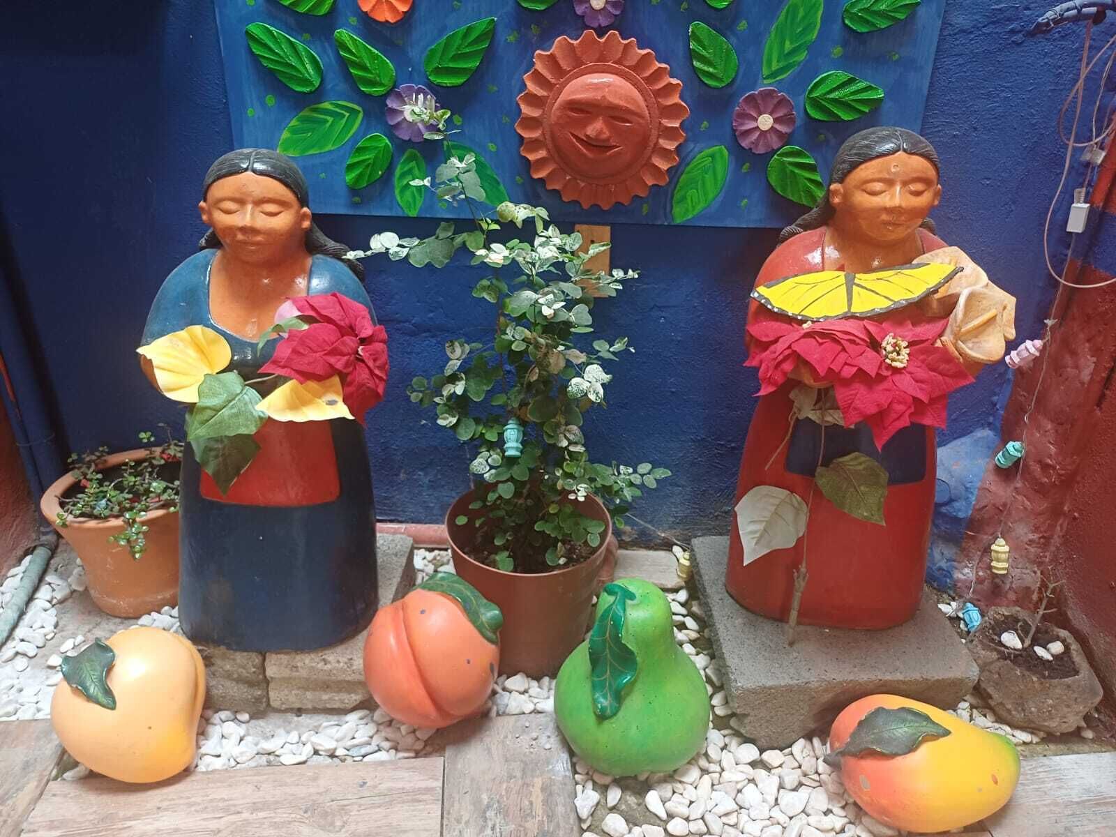 Two statues with potted plants, a wall with colorful decorations, and a small garden area.