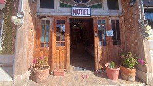 Un bâtiment en bois avec une enseigne indiquant « HÔTEL » au-dessus de l’entrée. Des plantes en pot sont disposées devant l’entrée.
