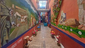 Un couloir étroit aux murs ornés de peintures murales colorées, avec des bancs en bois et des compositions florales disposées sur le sol.