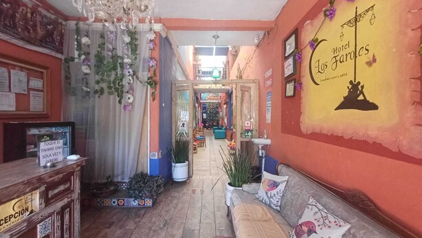 Un hall d’hôtel comprenant un comptoir d’accueil, un canapé avec des coussins, un lustre et un mur sur lequel est inscrit le nom de l’hôtel.