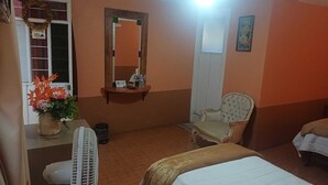 Une chambre d’hôtel avec un lit, une chaise, un bureau avec un ventilateur, un miroir et une fenêtre décorée d’une guirlande.