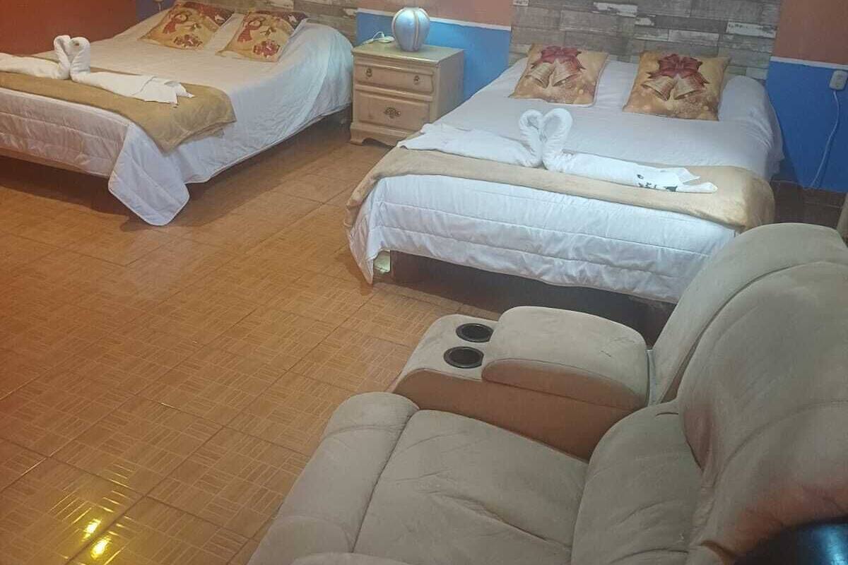 Habitación de hotel con dos camas, una silla de masaje, una mesita de noche con lámpara y decoración floral en la pared.