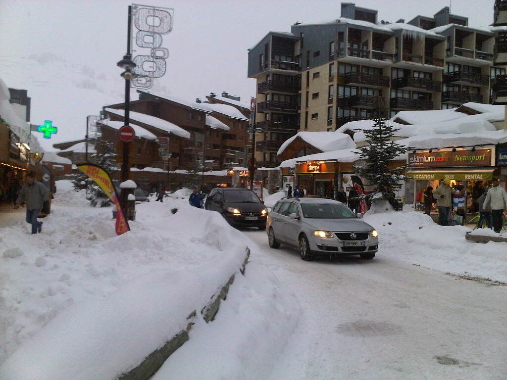 A snowy urban street with buildings, a car, and a sign for 'Ski Resort'.