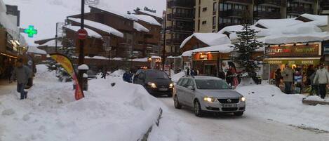 Una calle urbana nevada con edificios, un coche y un cartel que anuncia 'Ski Resort'.