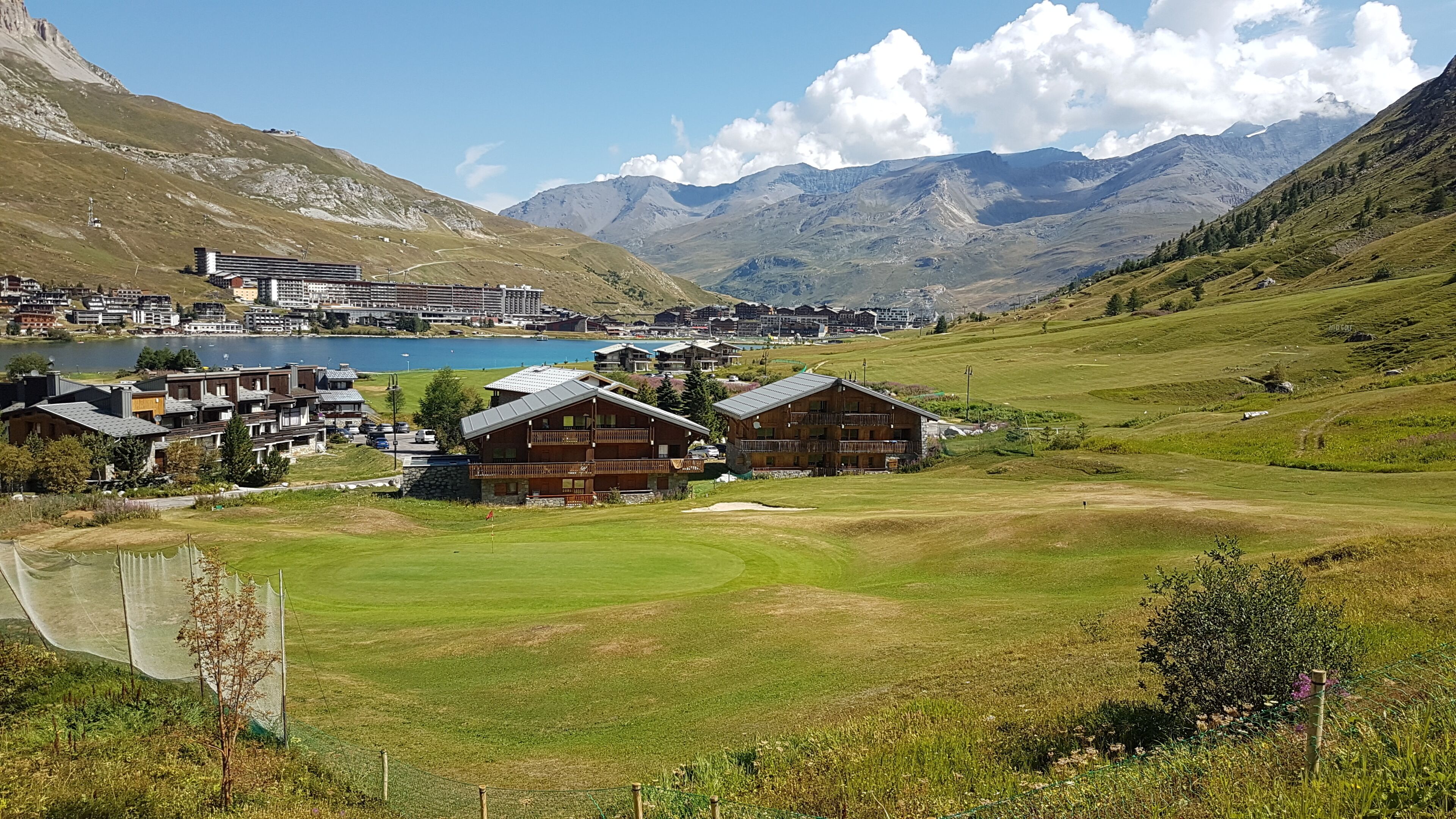 Un paisaje montañoso con un lago, un campo de golf y un grupo de edificios de madera con balcones.