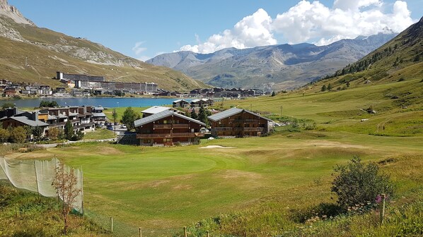A mountainous landscape with a lake, a golf course, and a cluster of wooden buildings with balconies.