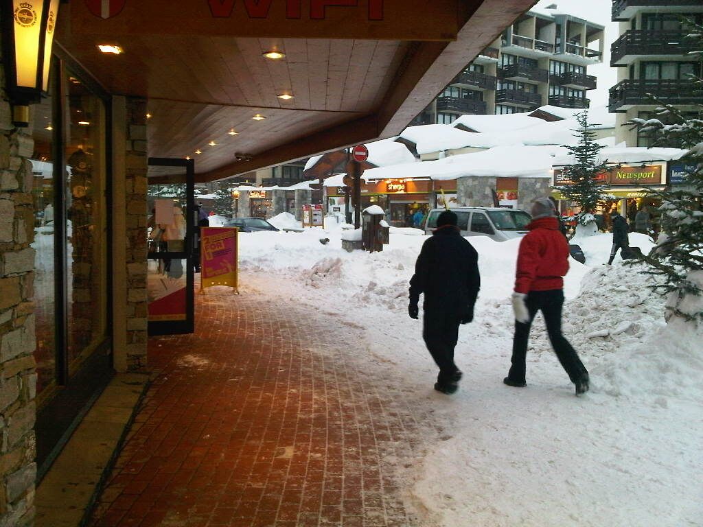 L'ingresso di un hotel con un vialetto in mattoni che conduce alla porta, un'area coperta con un cartello e una strada innevata con edifici e auto.