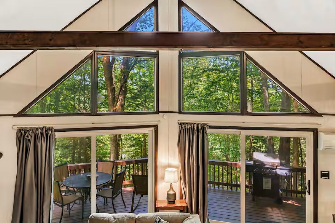 A room with a large window, a table with chairs, a lamp, and a grill outside.