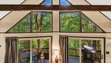 A room with a large window, a table with chairs, a lamp, and a grill outside.