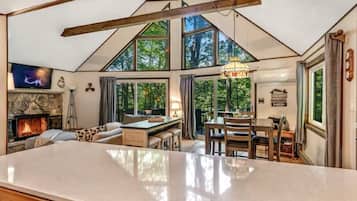 A spacious interior with a stone fireplace, a large dining table, and a view of the outdoors through large windows.