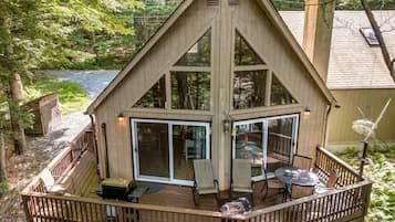 A wooden cabin with a deck, large sliding glass doors, and a small outdoor seating area.