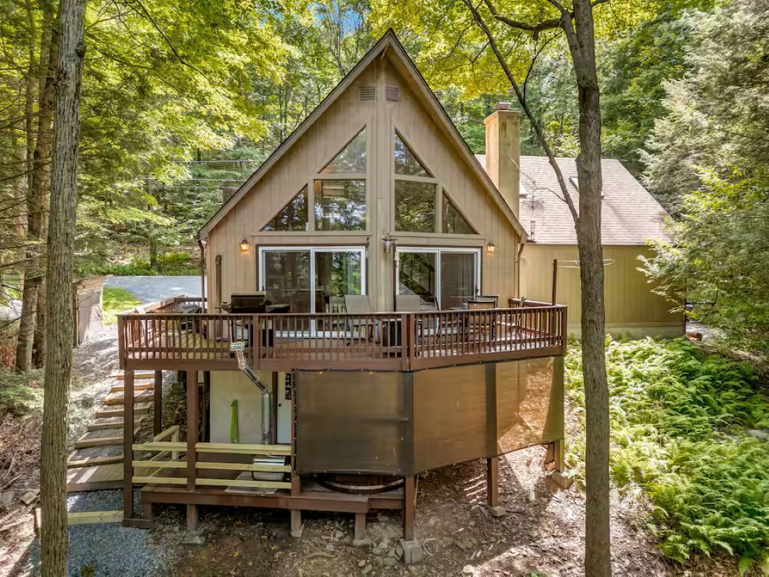 A cabin with a deck, a chimney, and a large window.