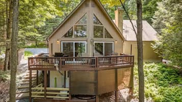 A cabin with a deck, a chimney, and a large window.