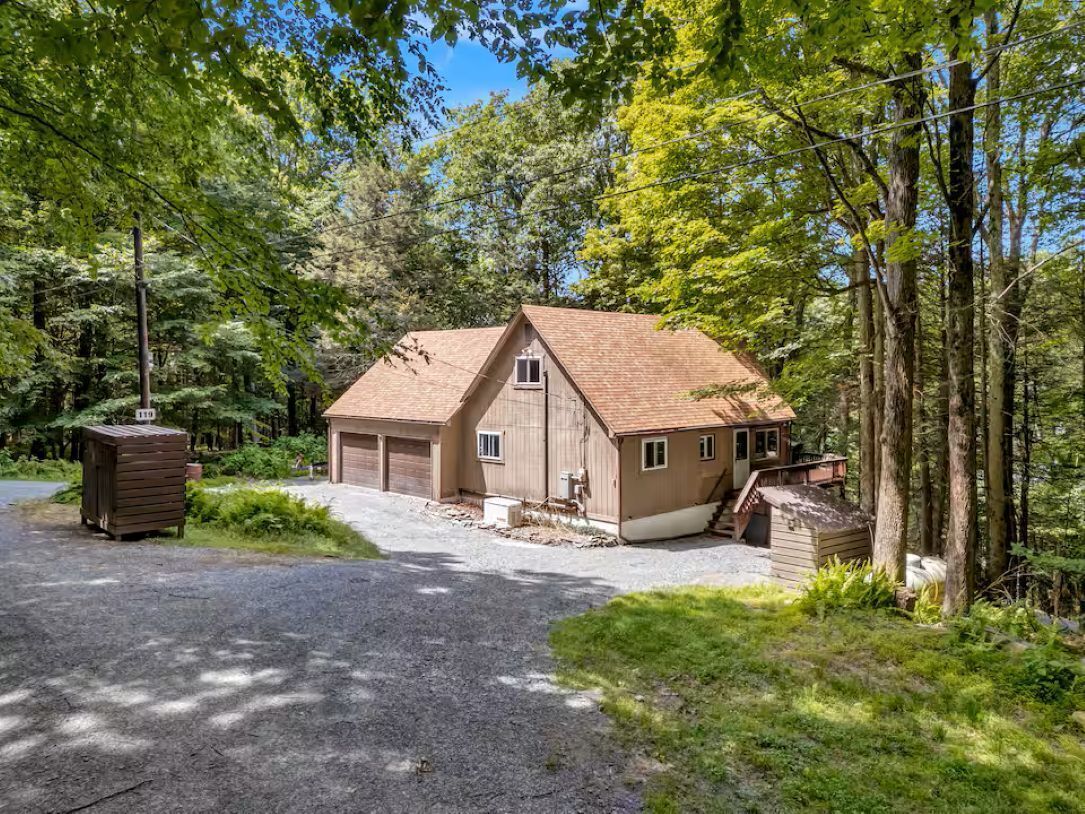 A two-story wooden cabin with a garage, surrounded by trees.