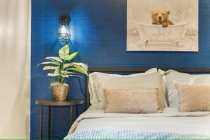 Ein Schlafzimmer mit blauer Wand, einem Nachttisch mit Pflanze, einer Lampe und einem Bild von einem Bären in der Badewanne.