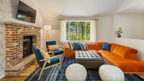 Un salón con chimenea de ladrillo, un sofá, una silla y un ventanal con vistas a zonas verdes.