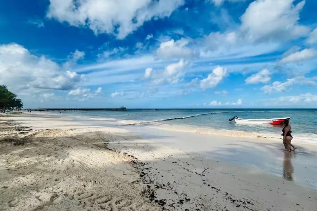 Une plage avec un bateau, un ciel dégagé et une jetée au loin.