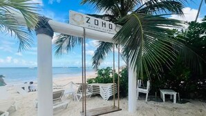 Ranta, jossa on keinuteline, kyltti, jossa lukee ”ZOHO”, ja palmu.