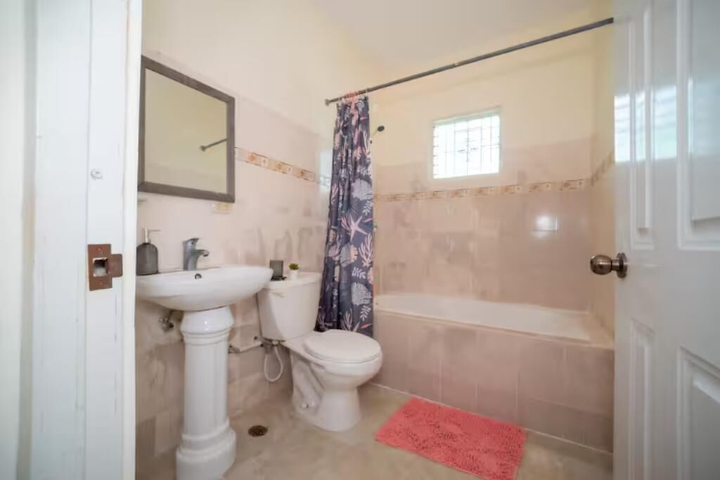 A bathroom with a pedestal sink, toilet, bathtub, and a shower curtain.