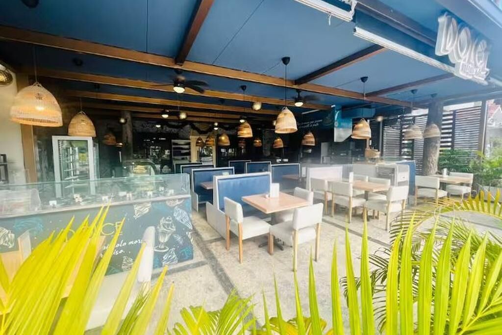 An outdoor seating area with tables and chairs, a glass partition, and hanging pendant lights.