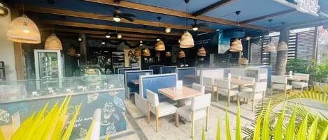 An outdoor seating area with tables and chairs, a glass partition, and hanging pendant lights.