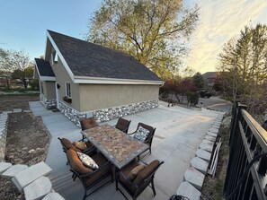 Eine Terrasse mit Tisch und Stühlen, eine Steinmauer und ein Haus mit Satteldach.