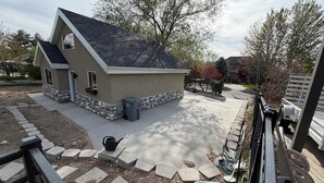 A house with a stone foundation, a grey roof, and a paved driveway.