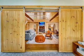A spacious living area with a fireplace, a television, and a dining area with wooden furniture. - Summitgrove Cabin w/ Hot tub, Game Room &OutdoorTV (Long Pond)