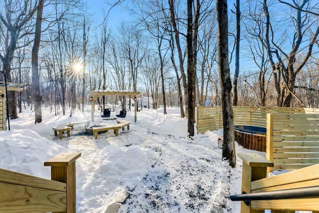 A snowy outdoor area with wooden benches, a covered seating area, and a wooden fence.