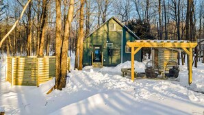 En træhytte med veranda og et lille skur i en snefyldt skov.