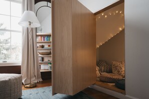 A cozy reading nook with a bookshelf, a lamp, and a window. - Luxury Lakeview Estate w/ Indoor Pool & Golf Sim (Ithaca)