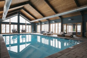 An indoor swimming pool with wooden beams, large windows, and seating areas. - Luxury Lakeview Estate w/ Indoor Pool & Golf Sim (Ithaca)