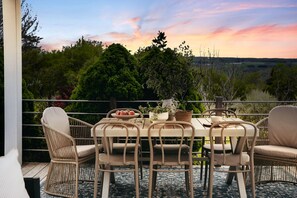 An outdoor dining area with wicker furniture and a table set for two, overlooking a natural landscape. - Luxury Lakeview Estate w/ Indoor Pool & Golf Sim (Ithaca)