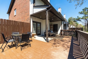 Une terrasse avec une table et des chaises, une plateforme en bois et, au fond, un bâtiment en briques.