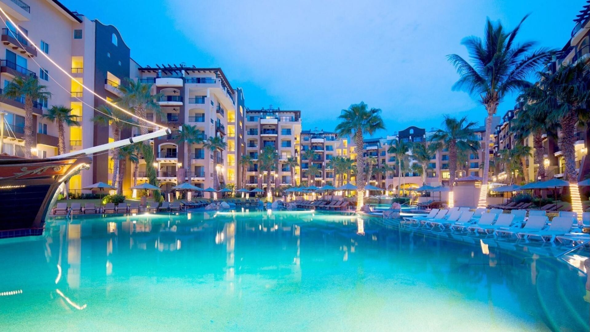 Et hotel med en stor pool omgivet af palmer og liggestole.