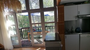 Een keuken met een eethoek, uitzicht door glazen deuren en een terras met een tafel en stoelen.