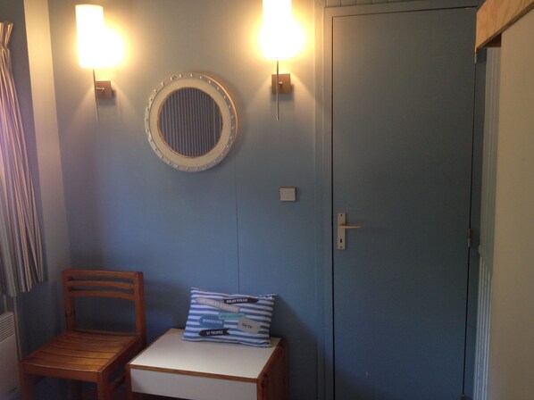 A room with a blue wall, a wooden chair, a small table, a pillow with text, a round mirror, and two wall-mounted lights.